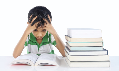 Young boy at desk with a printed books, hands on head, troubled look